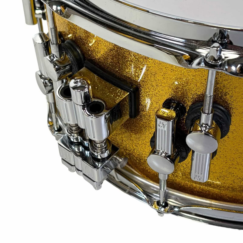 Snare drum with gold sparkle finish, featuring chrome hardware and precise tuning lugs.