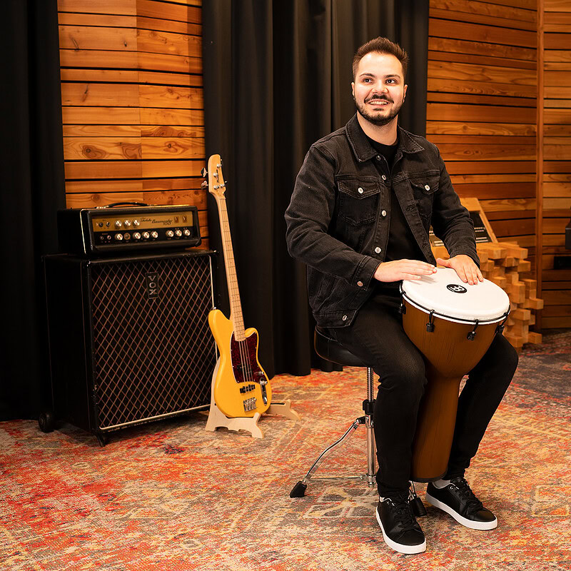 Young man playing conga drum in a professional music studio with guitars and piano.