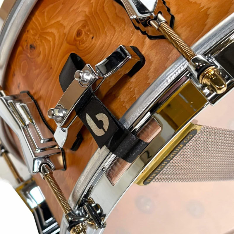 High-quality wooden snare drum with chrome hardware and black strap detail.