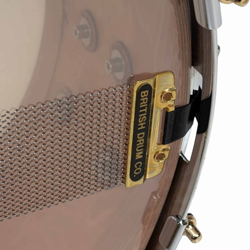 Close-up of British Drum Co 'The Archer' 14x6in snare drum with gold hardware and mesh grille.