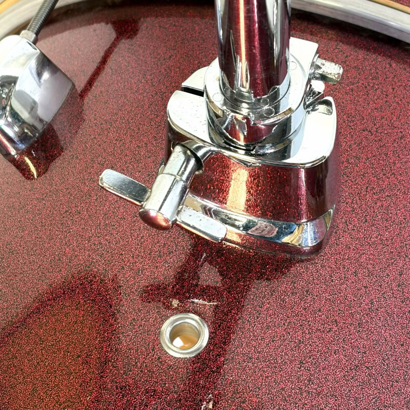 Close-up of drum kit hardware on a red textured surface, showcasing drum stands and mounting compone.
