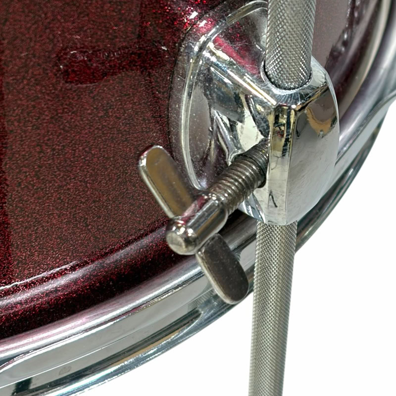 Close-up of drum kit hardware and tension rod on a red drum.