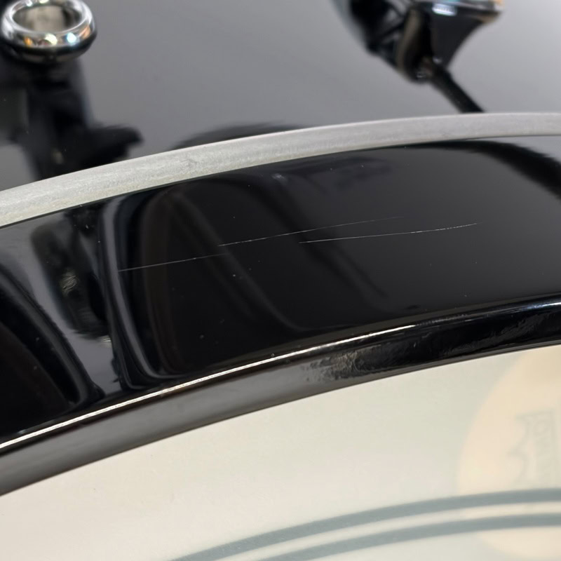 Close-up of Drummers Only logo on a black drum kit with minor surface scratches.