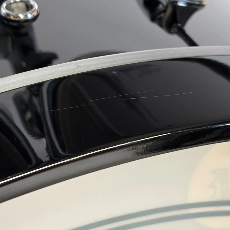 Close-up of Drummers Only logo on a black drum kit with minor surface scratches.