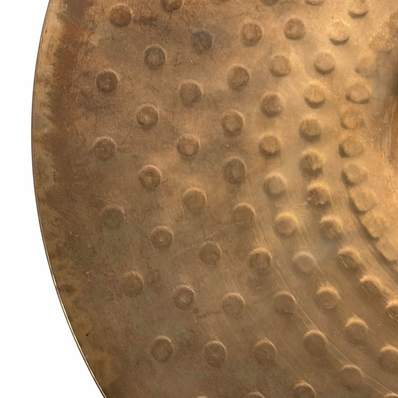 Close-up of a vintage cymbal with textured surface and rivets, used in drumming.