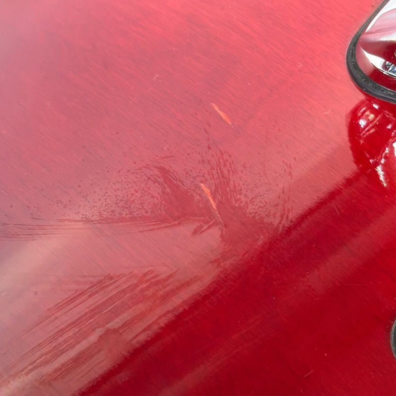 Scratch damage on a red car's body panel with visible paint scuffs and surface marks.