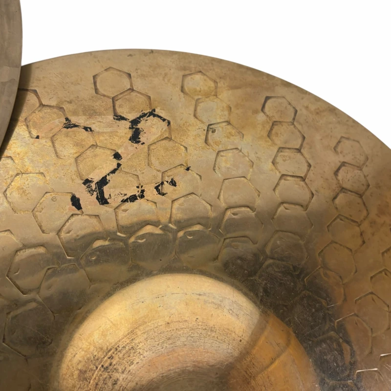 Close-up of a vintage drum cymbal with hexagonal pattern and signs of wear.
