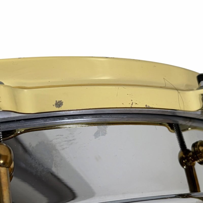 Close-up of a vintage snare drum with gold hardware and minor scratches.