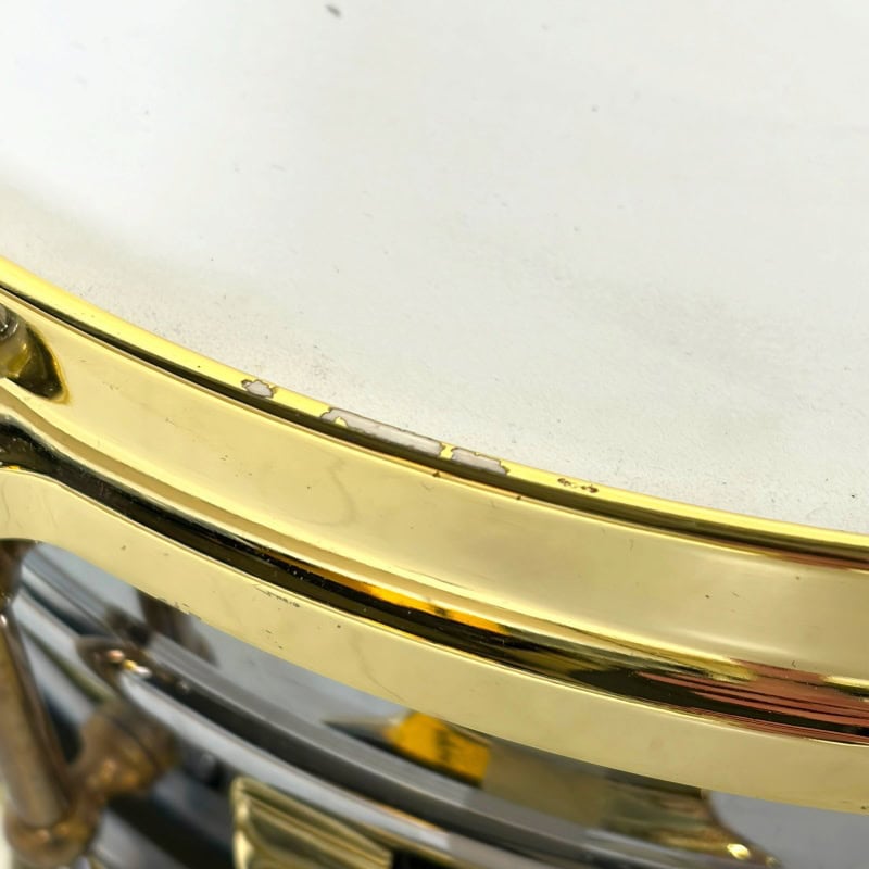 Close-up of a shiny gold drum snare with detailed hardware.
