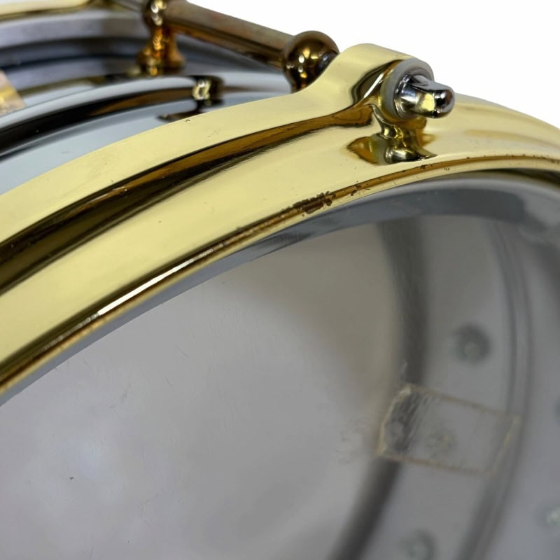 Close-up of a shiny gold snare drum, highlighting its polished surface and hardware.