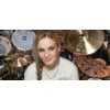 Female drummer smiling with drum kit and cymbals in a music studio.
