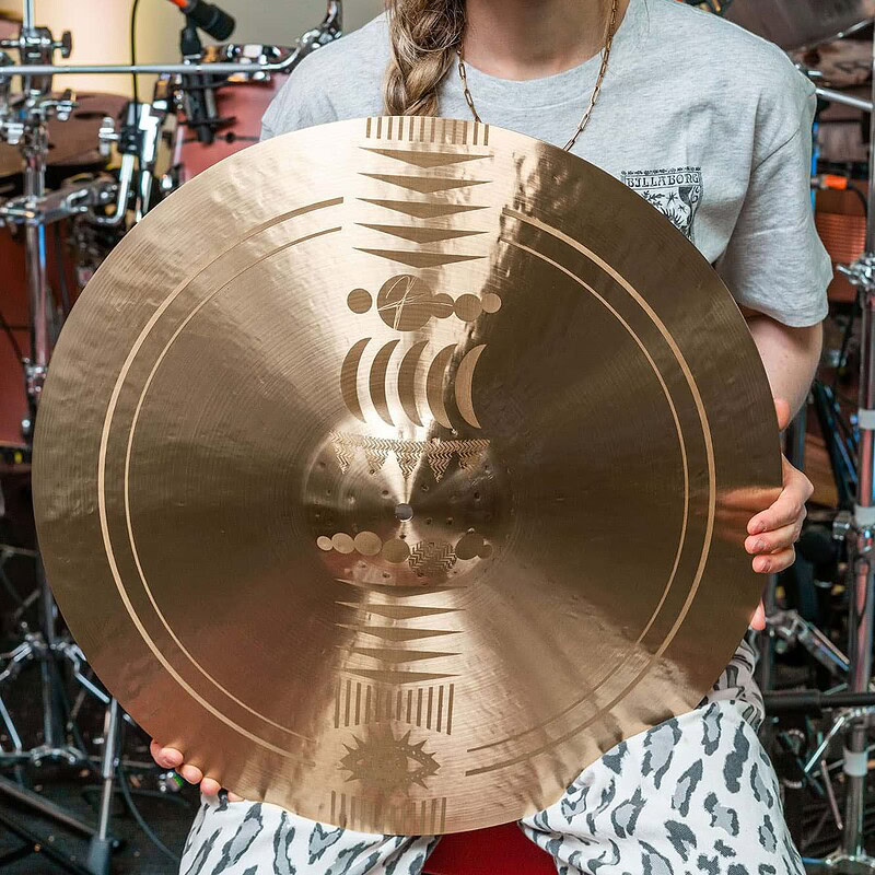 Female drummer holding a large cymbal in a professional drum studio.