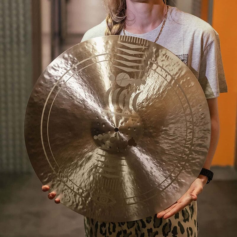 Female drummer holding a large cymbal in a music studio corridor.