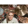 Female drummer smiling among various cymbals and drums in a music studio.