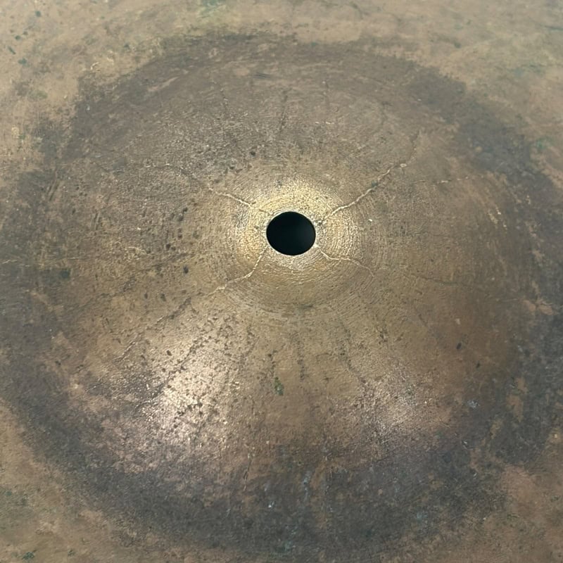 Close-up of a vintage ride cymbal with a central hole and patina finish.
