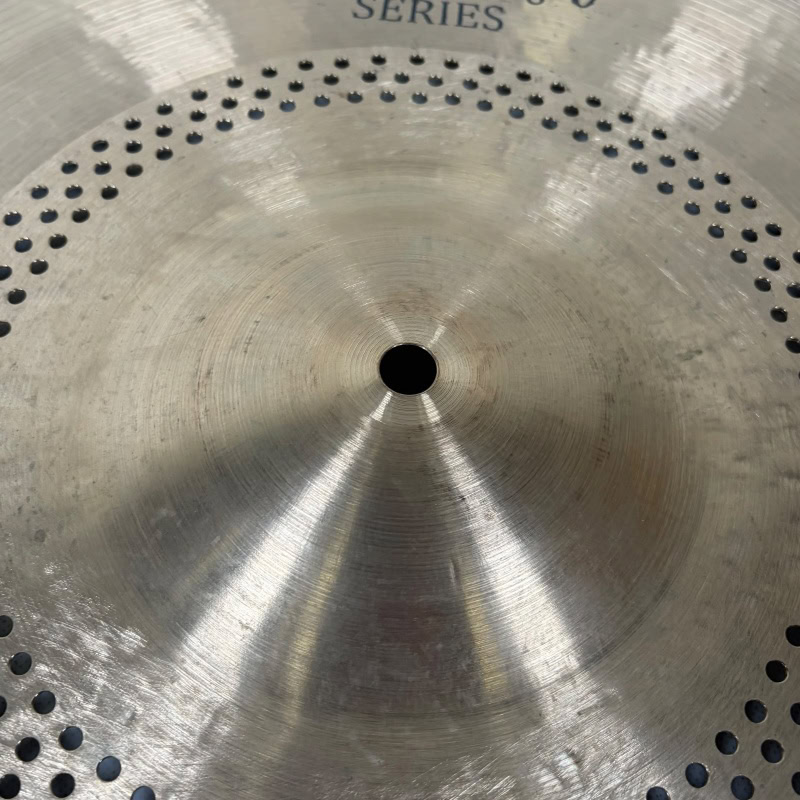 Close-up of a silver ride cymbal with perforations and a central hole.