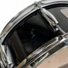 Close-up of a black snare drum with chrome hardware and drumsticks.